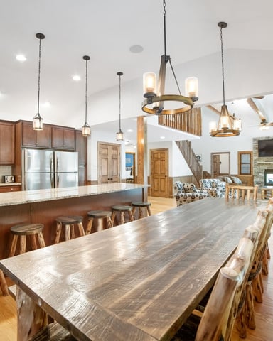 Open-plan kitchen and dining area with wood cabinetry, granite countertops, rustic dining table, and pendant lighting overlooking living room with fireplace.