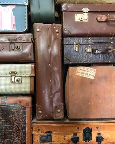 Stacked vintage leather suitcases in brown, tan, and blue with brass latches and handles