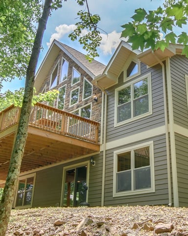 Modern two-story house with gray siding, large windows, and wooden deck nestled among tall trees