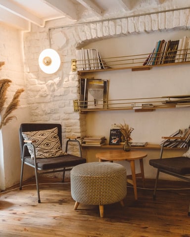 Living room with exposed brick walls, mid-century modern furniture, wooden shelves with books, and natural light from large window