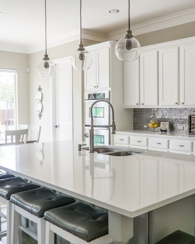 Modern kitchen with white cabinetry, gray subway tile backsplash, large island with black stools, and pendant lights overlooking dining area