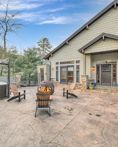 Concrete patio with hot tub, fire pit, Adirondack chairs, and modern shingle house with stone accents
