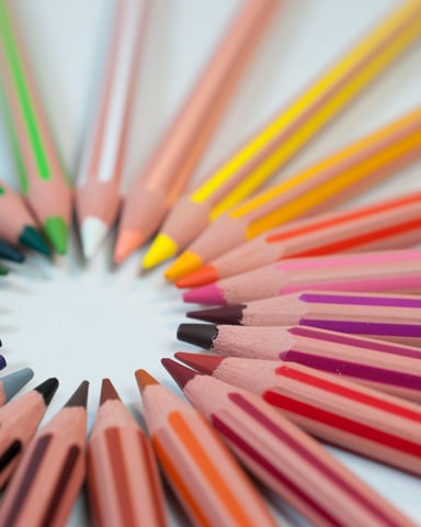 Colored pencils arranged in a circle with sharpened tips pointing inward, showing a rainbow of colors including blue, green, yellow, orange, red, pink, and