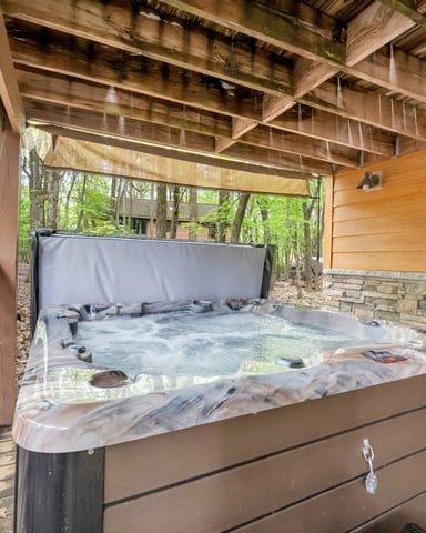 Covered wooden deck with hot tub, stone wall, and forest view