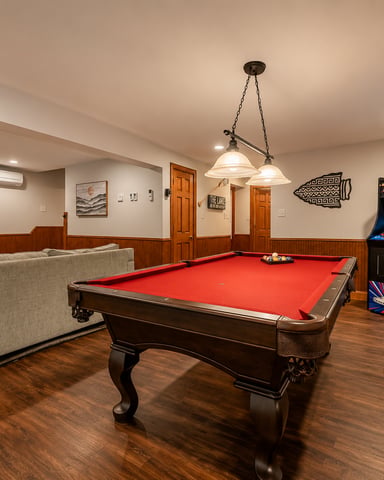 Finished basement with red pool table, fireplace, gray sofa, arcade game, and wood paneling