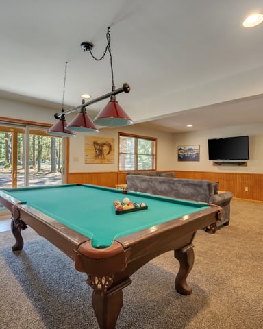 Recreation room with pool table, red pendant lights, wood paneling, TV, and glass doors opening to wooded deck