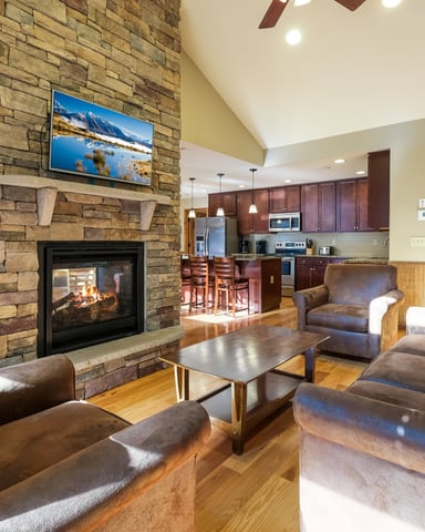 Open-plan living room with stone fireplace, leather seating, and kitchen visible in background