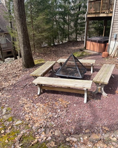 Wooded backyard with picnic table and fire pit surrounded by tall trees and cabin with deck
