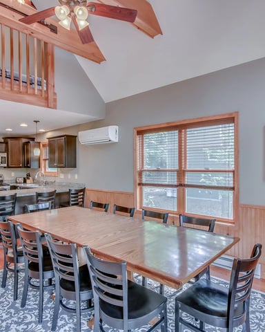 Open-plan dining and kitchen area with vaulted ceiling, wood beams, large windows, and hardwood floors