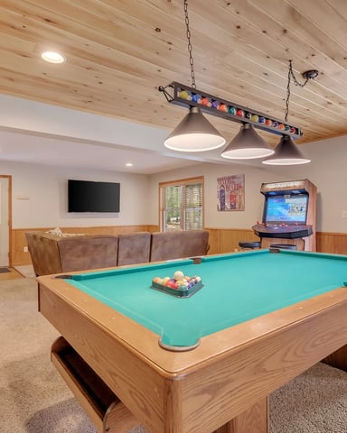 Recreation room with pool table, arcade game, brown leather seating, and wood-paneled walls with glass doors to outdoor patio.
