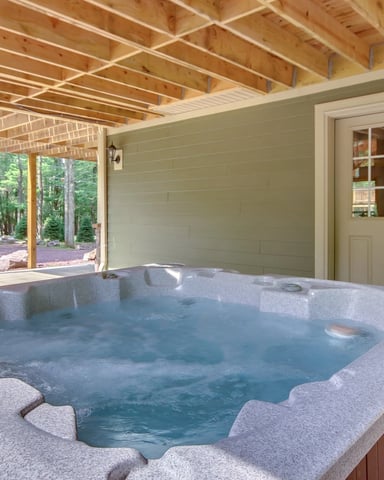 Hot tub in covered pavilion with exposed wood beams, green walls, and forest view through open side