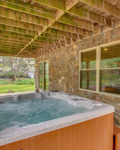 Covered hot tub with stone walls and wooden beams, overlooking backyard with trees