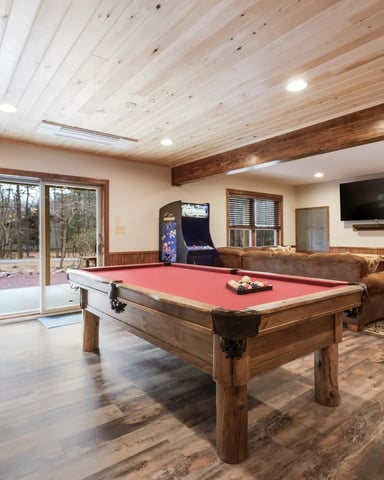 Game room with pool table, arcade machine, TV, wood beams, and glass doors opening to patio