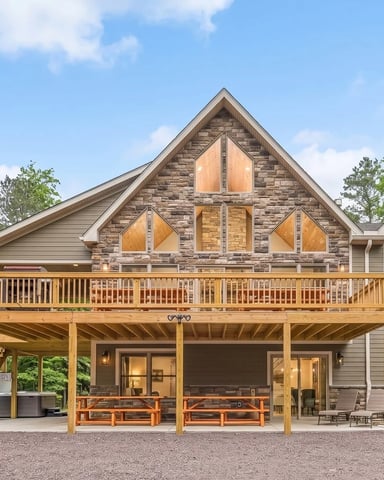 Modern stone and wood house with wraparound deck, covered patio, and large windows surrounded by trees