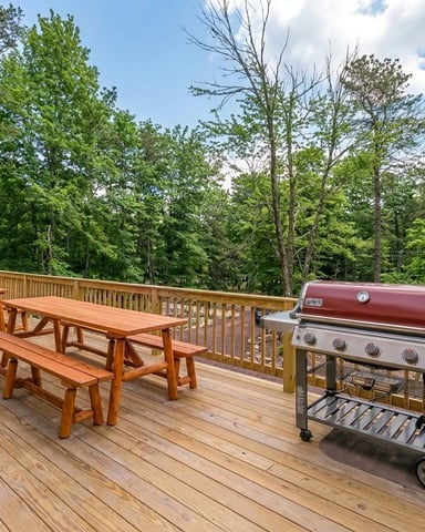 Wooden deck with picnic table, benches, gas grill, and forest view beyond railing