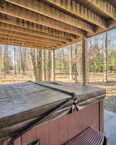 Covered patio with hot tub overlooking bare autumn trees and wooded grounds