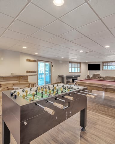 Game room with foosball table, pool table, wooden bar seating, and flat-screen TVs