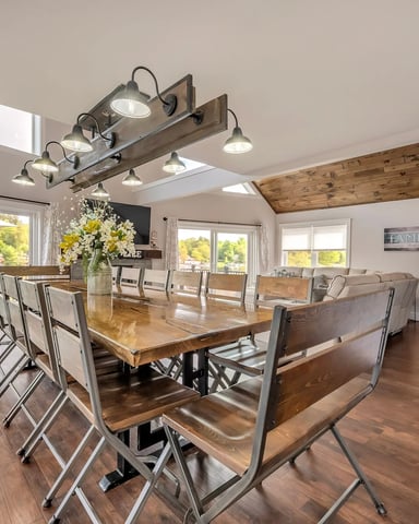 Open-plan dining and living room with wood table, metal chairs, skylights, and views of green landscape through glass doors