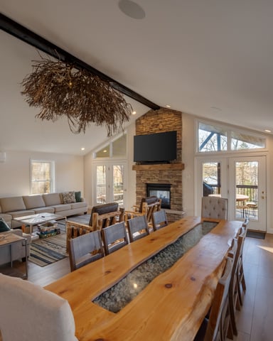 Open-plan living and dining area with wood table, fireplace with TV, gray sofa, and glass doors to deck