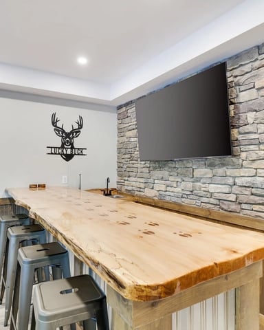 Game room with wood bar, metal stools, stone accent wall, flat-screen TV, and deer head wall decal