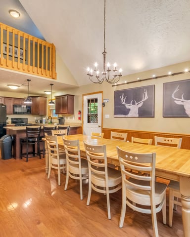 Open-plan dining and kitchen area with wood flooring, dining table, deer artwork, and loft space above.