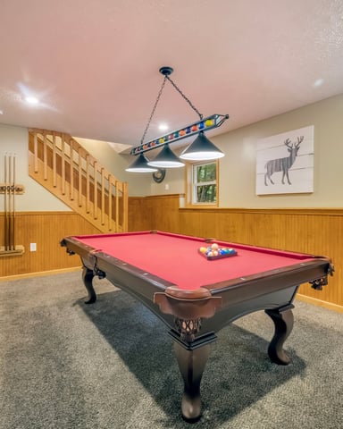 Basement recreation room with red pool table, wooden paneling, staircase, and wildlife wall art