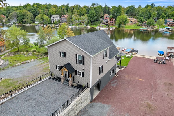Waterfront house with gray siding and dark roof on river, surrounded by trees and neighboring homes across the water.