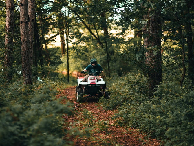 Person riding an ATV alone through a sun-dappled forest trail