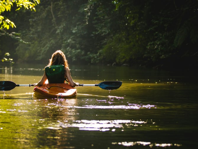 Woman kayaking alone on a calm green river through dense forest
