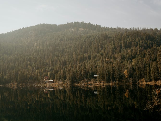 Cabin reflected in a still mountain lake surrounded by pine forest