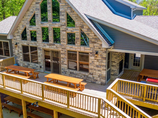 Modern stone house with yellow deck, multiple levels, picnic tables, and wooded surroundings