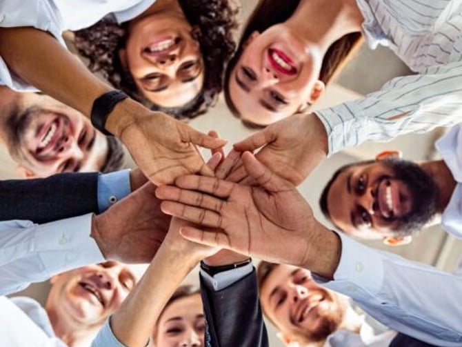 Group of diverse people stacking hands together in circle, smiling at camera from below